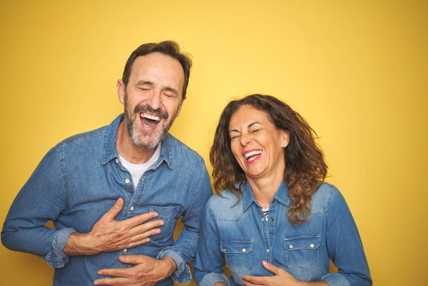 Mooie Middeleeuwen paar samen staande over geïsoleerde gele achtergrond glimlachen en lachen hard uit luid omdat grappig gekke grap met handen op lichaam. - Foto, afbeelding