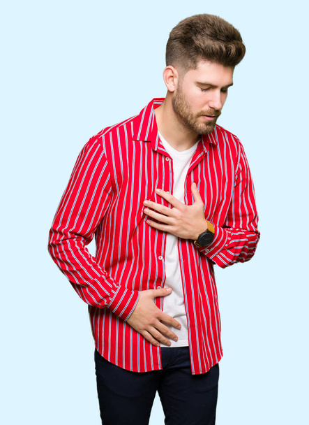 Jeune bel homme portant une chemise rouge avec la main sur le ventre parce que l'indigestion, la maladie douloureuse se sent mal. Concept Ache
. - Photo, image
