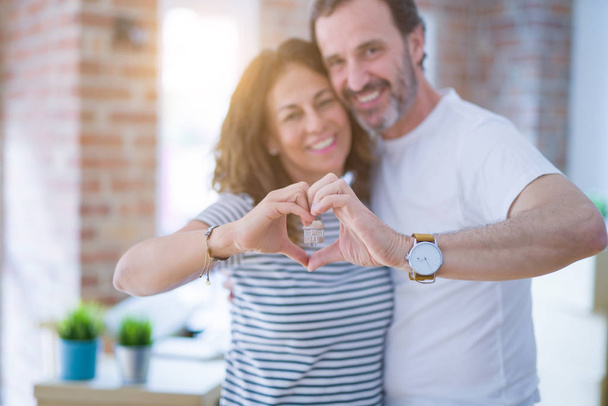 Middle age senior romantic couple holding and showing house keys, doing heart shape with hands smiling happy for moving to a new home - Foto, Imagem