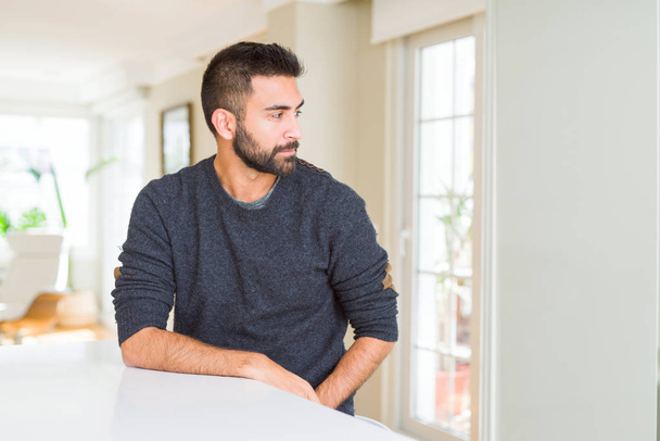 Hombre hispano guapo usando suéter casual en casa mirando al costado, pose de perfil relajado con cara natural con sonrisa confiada
. - Foto, imagen