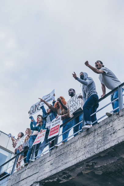 vista de ángulo bajo del grupo multicultural de personas gritando y haciendo gestos mientras sostiene pancartas
  - Foto, Imagen