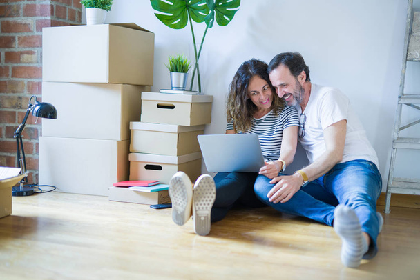 Старша романтична пара середнього віку закохана, сидячи на підлозі квартири з коробками навколо і використовуючи комп'ютерний ноутбук, посміхаючись щасливим для переїзду в новий будинок
 - Фото, зображення