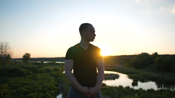 Bátor ember áll a terpeszes módon fordult a fejét félre tó naplementekor a slo-Mo - Felvétel, videó