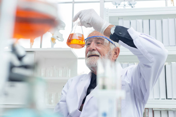 Científico sénior sosteniendo una muestra de sustancia química en su mano
. - Foto, Imagen