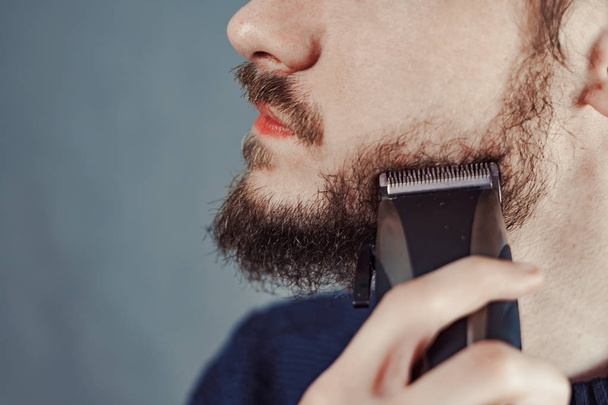 guy shaves his beard with an electric razor - Фото, зображення