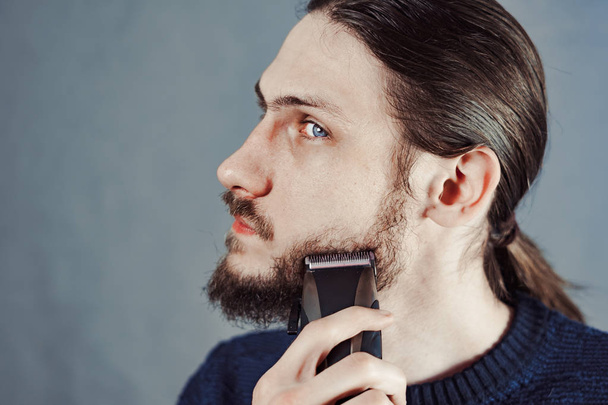 guy shaves his beard with an electric razor - Foto, afbeelding