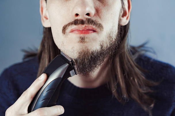 Guy scheert zijn baard met een elektrisch scheermesje - Foto, afbeelding