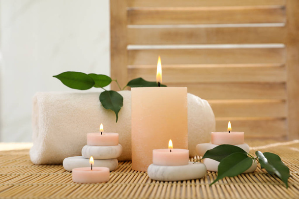 Composition of spa stones, towel and burning candles on bamboo mat - Foto, Imagem
