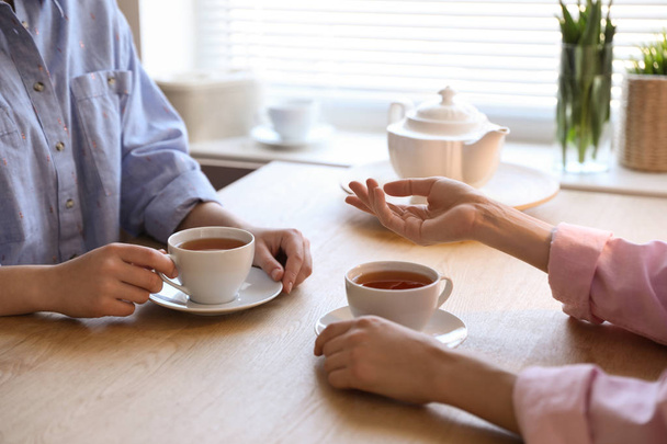 Women with cups of tea at table near window indoors, closeup - Photo, Image