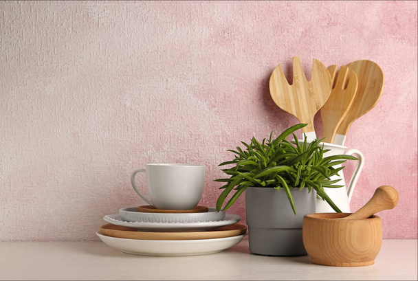 Green plant and different kitchenware on table near color wall, space for text. Modern interior design - Foto, Bild