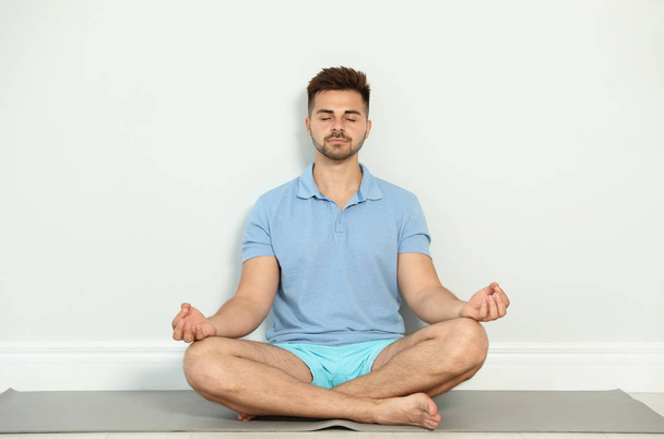 Jeune homme pratiquant le yoga zen près du mur à l'intérieur
 - Photo, image