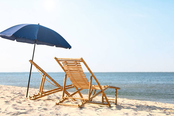 Empty wooden sunbeds and umbrella on sandy shore. Beach accessories - Foto, Imagen