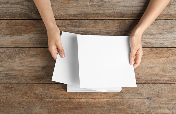 Žena, která drží prázdné papírové listy pro brožuru na dřevěném stole, pohled shora. S předstíranou - Fotografie, Obrázek