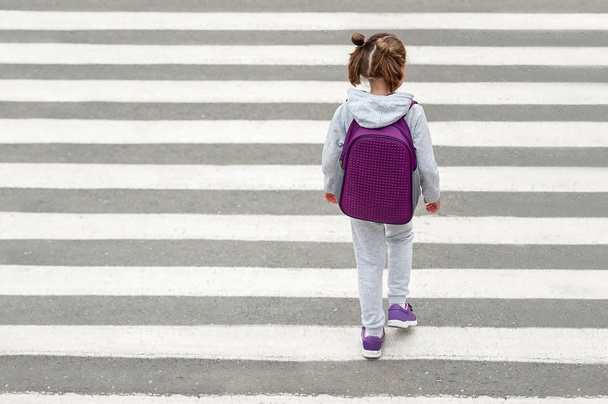 Schoolgirl crossing road on way to school. Zebra traffic walk way in the city. Concept pedestrians passing a crosswalk. Stylish young teen girl walking with backpack. Active child. Top view - Фото, зображення