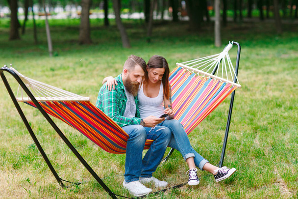 Young couple with mobile phone sitting on hammock. - Фото, зображення