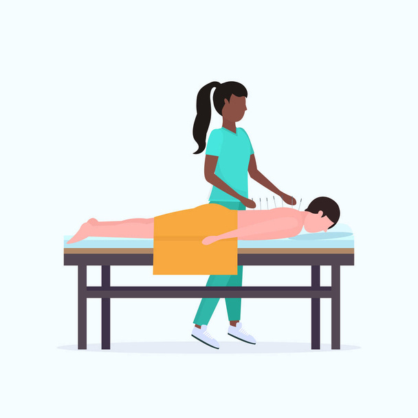 アフリカ系アメリカ人鍼医は、ベッド治療の上に横たわってリラックス鍼治療の男を得る針の男性患者を保持し、代替医療の概念を完全な長さ - ベクター画像