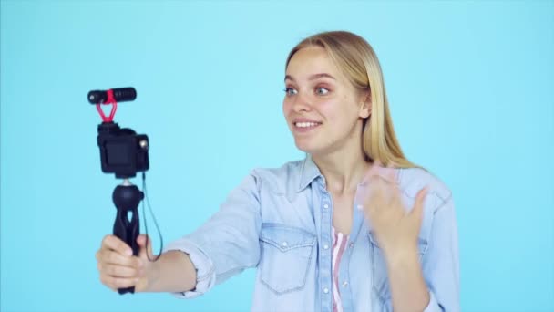 Bella ragazza blogger si solleva a macchina fotografica isolato sfondo blu - Filmati, video
