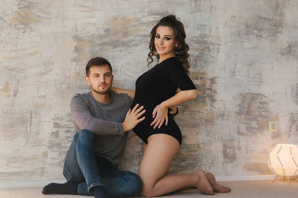 Happy man put his handr on the belly of his pregnant wife. Young family in studio. Couple wait for a baby - Foto, Imagem