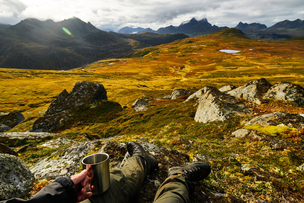 Man holding a cup of coffee with golden landscapes in the background on Lofoten Islands - Photo, Image