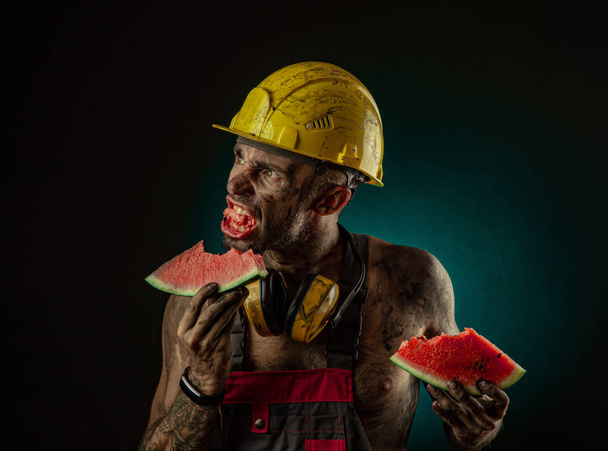 Portrét šťastného usmívajícího se horníka, který žere meloun na oběd - Fotografie, Obrázek