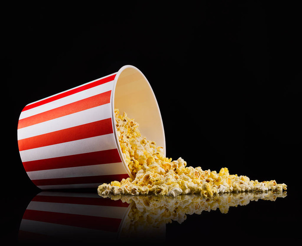 Scattered popcorn from paper striped bucket isolated on black background - Foto, imagen