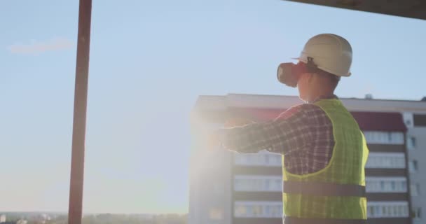 Ingenieur bouwer op het dak van het gebouw bij zonsondergang staat in vr-bril en beweegt zijn handen met behulp van de interface van de toekomst. Futuristische ingenieur van de toekomst. Het uitzicht vanaf de achterzijde. - Video