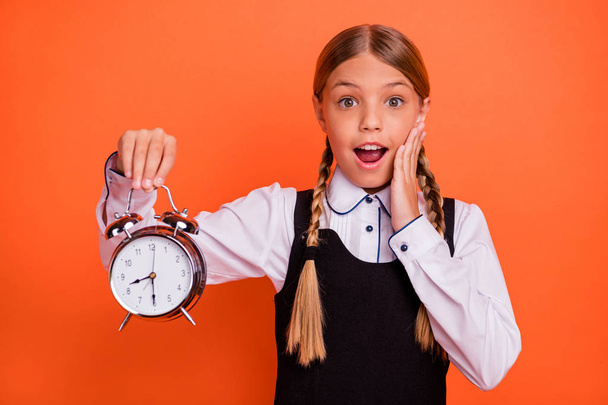 Close-up portrait of her she nice attractive lovely funny cheerful cheery glad pre-teen blonde girl holding in hand retro clock 1 September wakeup early isolated on bright vivid shine orange - Photo, image