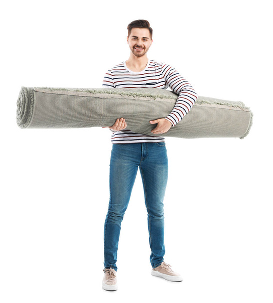 Young man holding rolled carpet against white background - Φωτογραφία, εικόνα