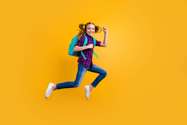 Full length side photo of little pupil jump high glad return school wear casual checkered shirt jeans denim isolated yellow background - Fotoğraf, Görsel