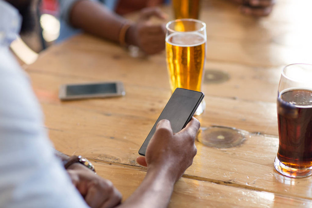 man with smartphone drinking beer at bar or pub - Fotó, kép