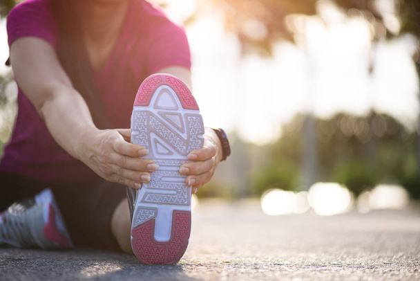 Jovem corredor mulher fitness sentar na estrada esticando as pernas antes de correr no parque. Conceito de atividades de exercício ao ar livre
. - Foto, Imagem
