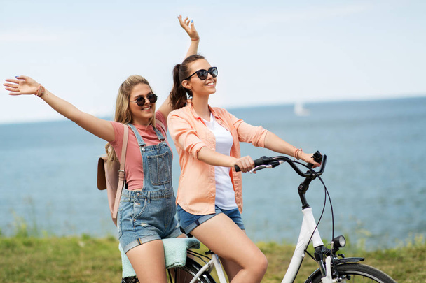 teenage girls or friends riding bicycle in summer - Fotoğraf, Görsel