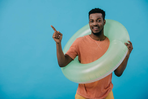 hombre africano americano positivo que está parado con el anillo inflable y que señala con el dedo aislado en azul
  - Foto, imagen