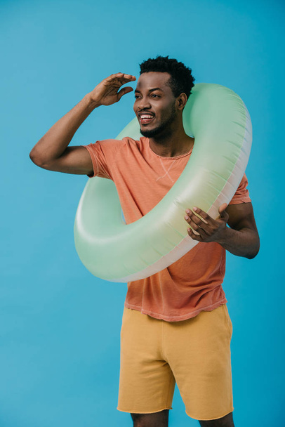 cheerful african american man gesturing while  standing with swim ring isolated on blue  - Fotografie, Obrázek