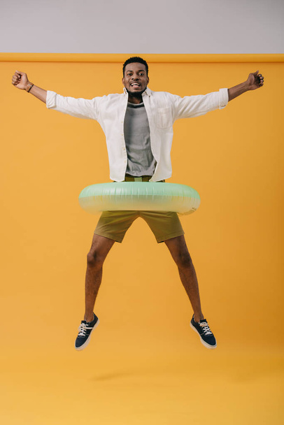 Gelukkig Afro-Amerikaanse man springen met zwemmen ring op oranje - Foto, afbeelding