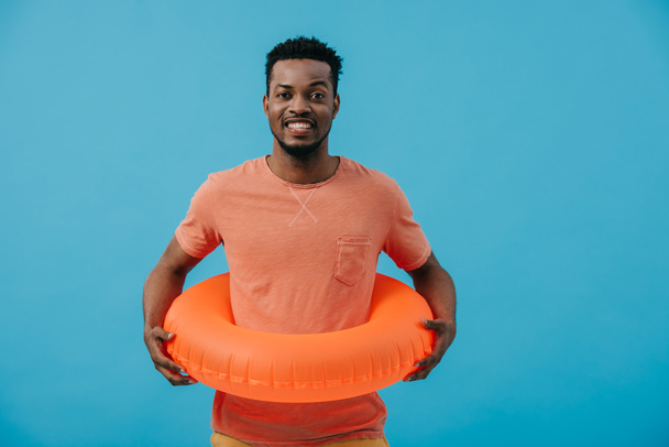 smiling african american man standing with inflatable ring isolated on blue  - Foto, imagen