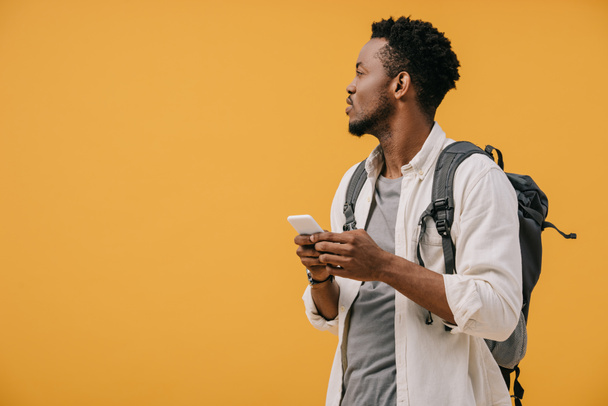 handsome african american man with backpack holding smartphone isolated on orange - Foto, Imagem