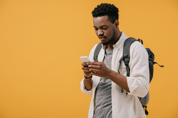 handsome african american man with backpack using smartphone isolated on orange - Foto, immagini