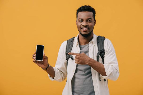 happy african american man with backpack pointing with finger at smartphone with blank screen isolated on orange - Φωτογραφία, εικόνα