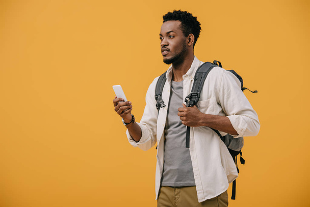 african american man with backpack holding smartphone isolated on orange - Foto, immagini
