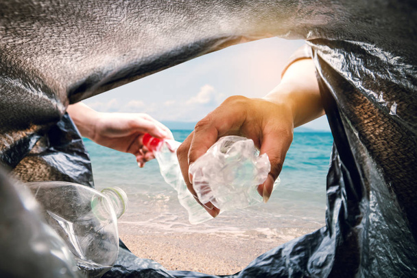 The volunteer picking up a bottle plastic in to a bin bag and the sea background ,recycling and protect environment from a pollution concept. - Foto, Imagen