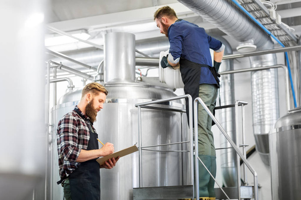 men with clipboard at brewery kettle or beer plant - 写真・画像