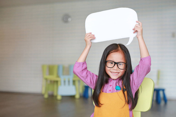 Adorable Asian little girl holding empty blank speech bubble to say something in the classroom with smiling and looking straight at camera. Education and conversation concept. - Foto, Imagem