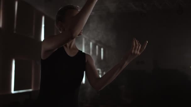 Prima Ballet Company in een donkere jurk op een donker theater podium repetising in de rook voert dansmoves in slow motion - Video