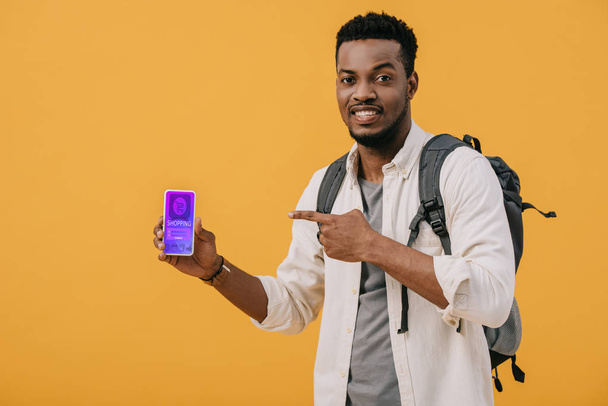 cheerful african american man pointing with finger at smartphone with shopping app on screen isolated on orange  - Foto, Imagem