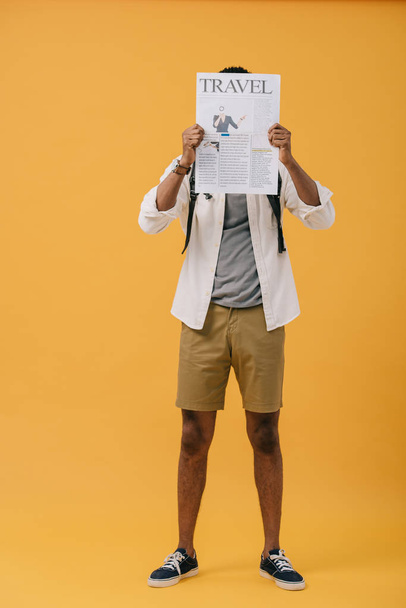 uomo afroamericano in piedi e volto di copertura con giornale di viaggio su giallo
  - Foto, immagini