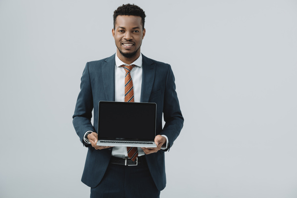 cheerful african american man holding laptop with blank screen isolated on grey  - Photo, Image