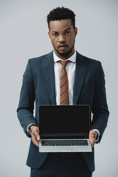 handsome african american man holding laptop with blank screen isolated on grey  - Valokuva, kuva