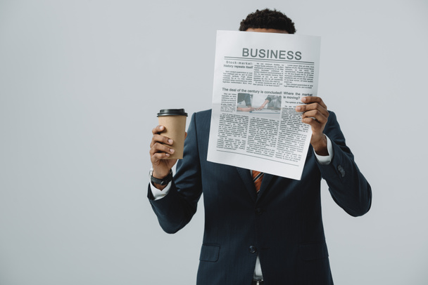 african american man holding disposable cup and covering face while reading business newspaper isolated on grey  - Photo, Image