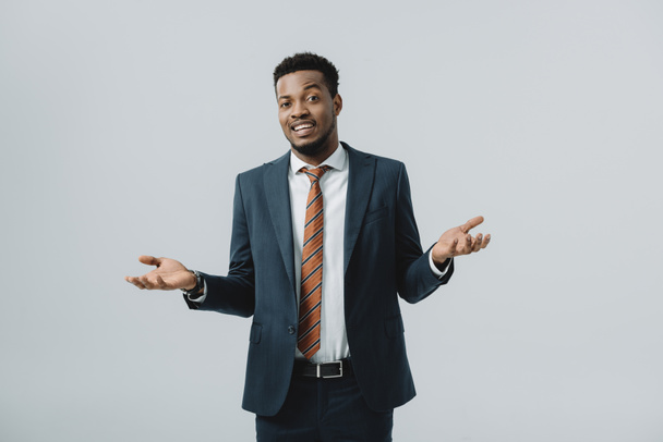 happy african american man showing shrug gesture isolated on grey  - 写真・画像